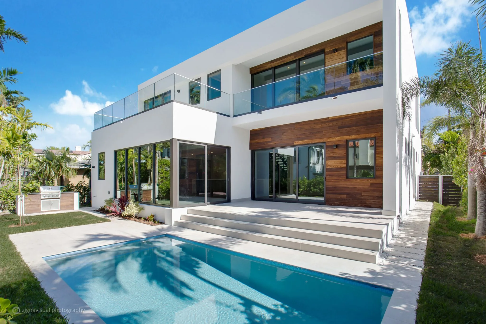 Rear exterior of contemporary two-story Miami Beach home with pool, terrace, wood cladding and glass balcony, Residential Architecture by Atelier International LLC